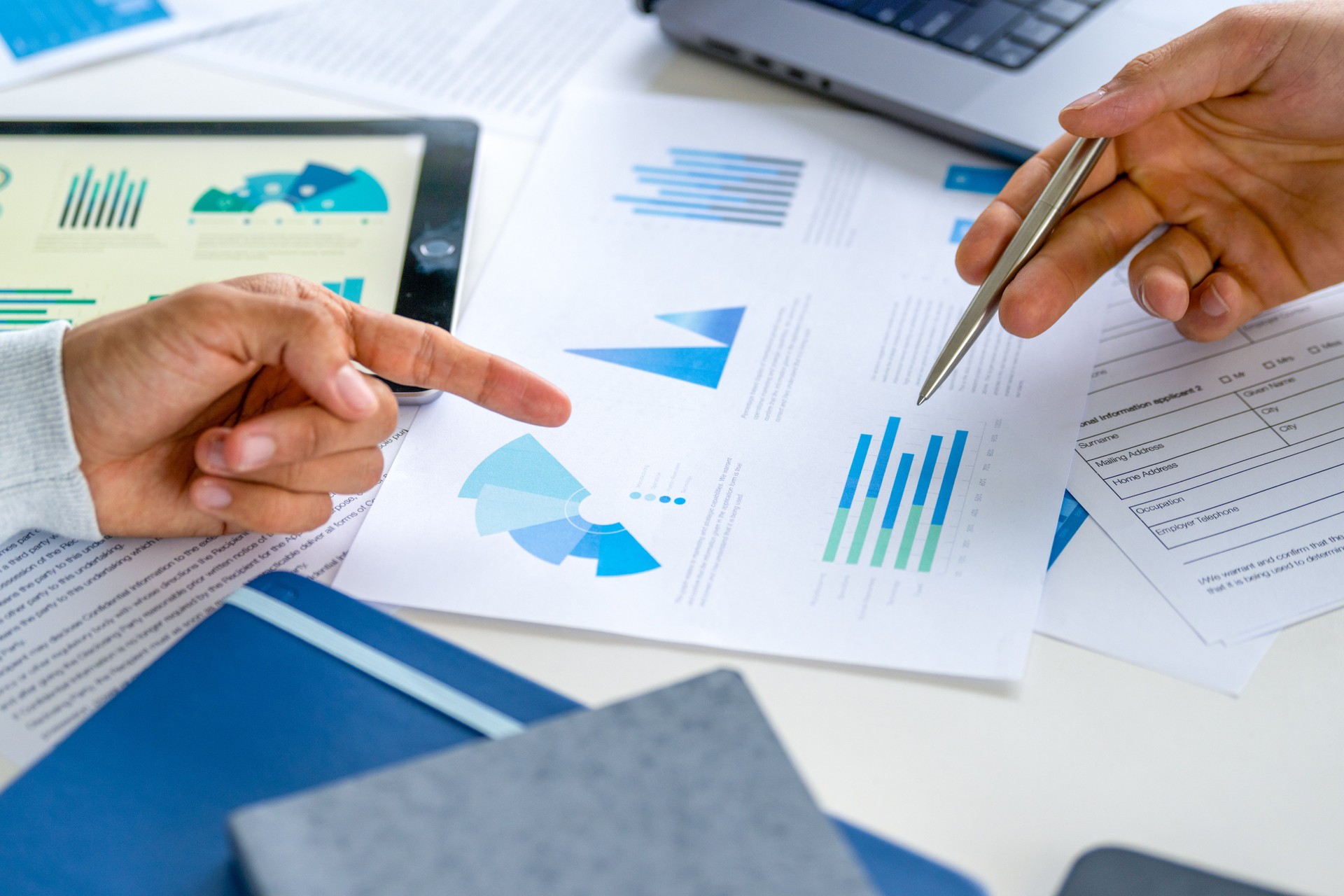 Two business men meeting and looking at financial data, charts and graphs on a digital tablet and paperwork documents